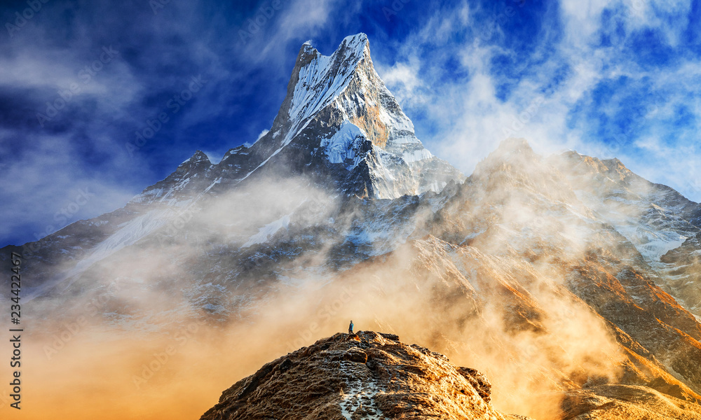 Hiker reaches the summit of mountain peak of Machapuchare. A mountain in the Annapurna Himalayas of north central Nepal. View point from Mardi Himal base camp track - obrazy, fototapety, plakaty 