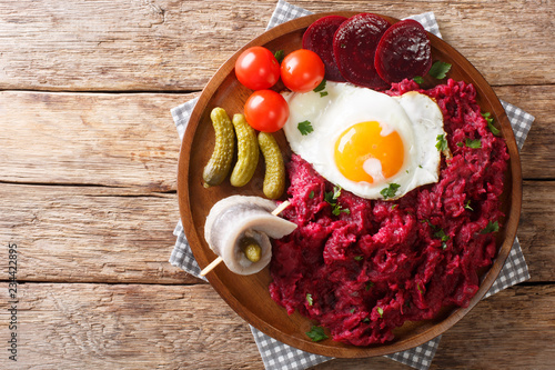 German cuisine Labskaus is a mashed potato, corned beef and beetroot with fried egg, pickled cucumbers and rollmop close-up. horizontal top view photo