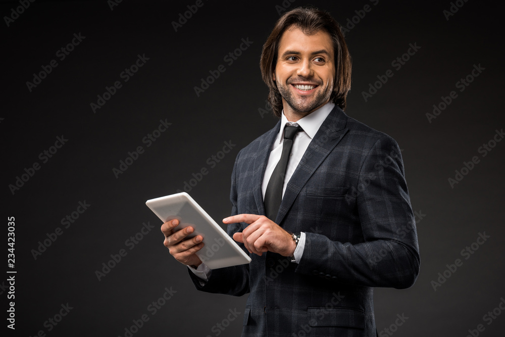 smiling young businessman using digital tablet and looking away isolated on black smiling young businessman using digital tablet and looking away isolated on black