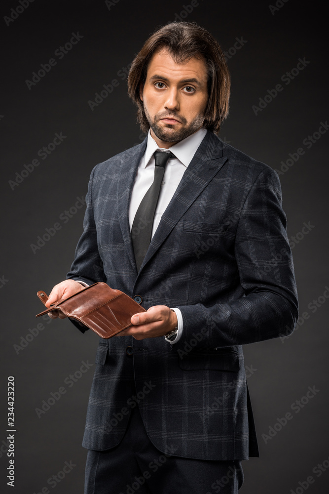 upset businessman holding empty wallet and looking at camera isolated on black