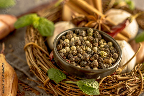 Mix of red  black and white pepper in a black bowl close-up against the background of chili pepper  garlic  cinnamon  onion and other spices