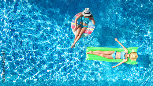 Aerial drone view of children in swimming pool from above, happy kids swim on inflatable ring donut and mattress, girls have fun in water on family vacation on holiday resort 