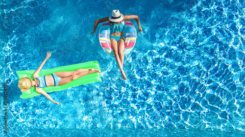 Children in swimming pool aerial drone view fom above, happy kids swim on inflatable ring donut and mattress, active girls have fun in water on family vacation on holiday resort
