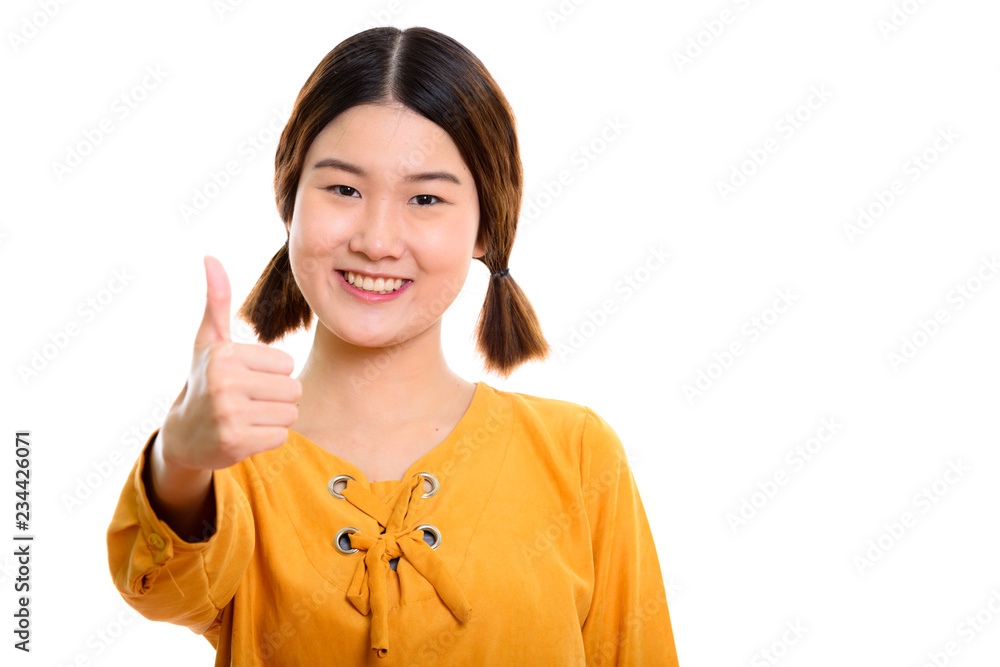 Studio shot of young happy Asian woman smiling while giving thum Studio shot of young happy Asian woman smiling while giving thum