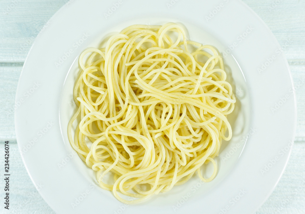 Yellow long spaghetti in a white plate on white wood background.