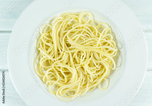 Yellow long spaghetti in a white plate on white wood background.