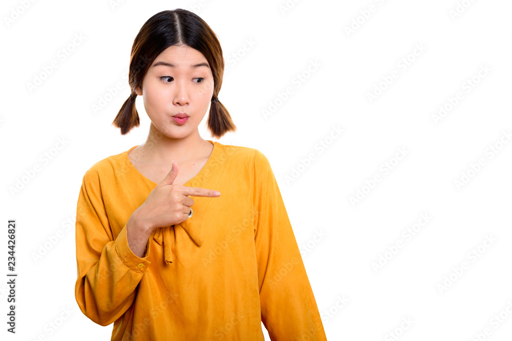 Studio shot of young beautiful Asian woman pointing finger to th Studio shot of young beautiful Asian woman pointing finger to th