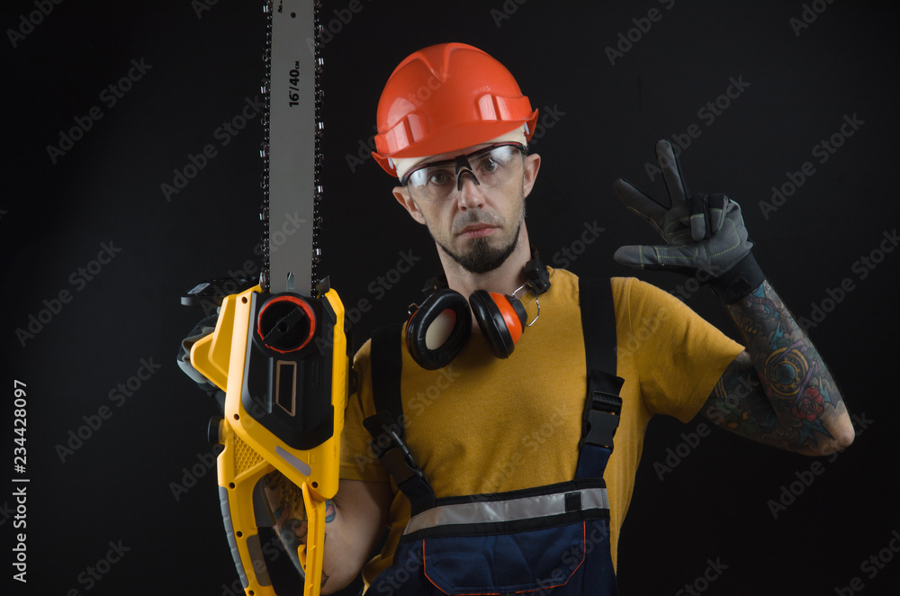 Fototapeta premium a young man posing on a black background in a work uniform and a construction tool