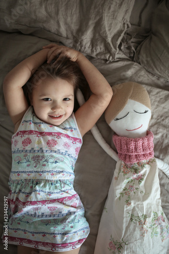 Toddler girl with soft handmade doll in bedroom