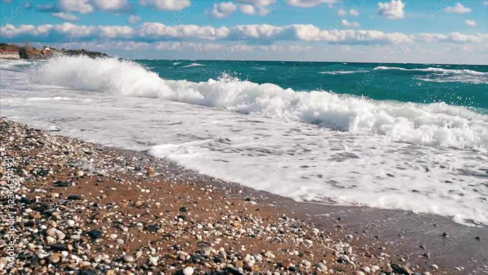 Sea wave crashing on sandy beach and cloudy blue sky background and birds flying over the sea Sea wave crashing on sandy beach and cloudy blue sky background and birds flying over the sea