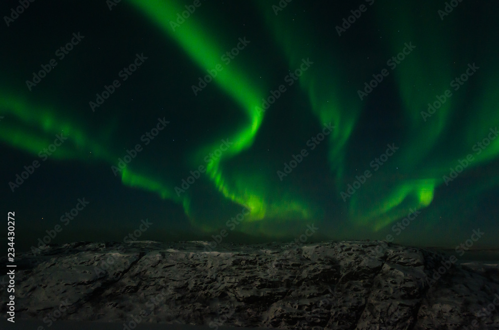 Beautiful stripes of the northern lights, aurora in the night sky above the snow covered hills.