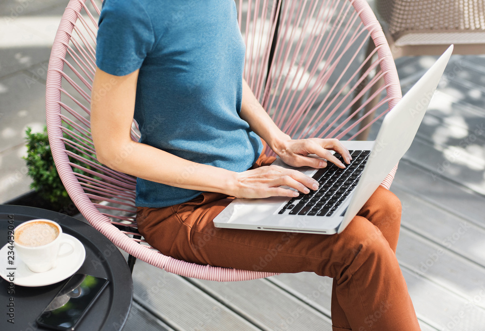 Naklejka premium Young woman using laptop outdoor. Creative professional girl sitting in a city cafe and working on computer