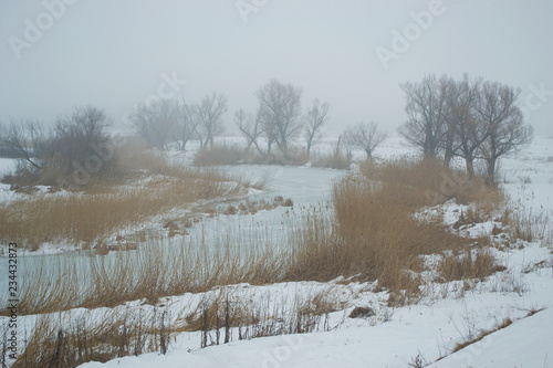 Winter landscape of foggy and frozen river with trees in the morning, from above view © vitusia