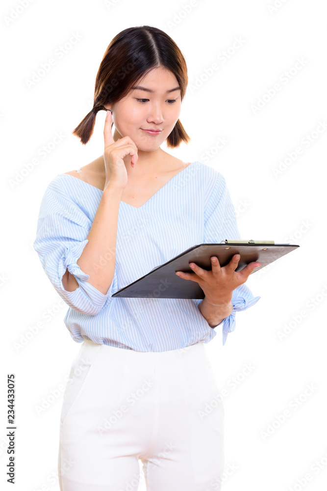 Young beautiful Asian woman reading on clipboard while thinking Young beautiful Asian woman reading on clipboard while thinking