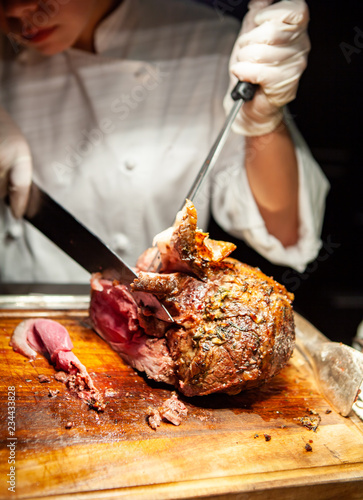 Professional chef carves a whole, roasted leg of lamb. An impressive centerpiece for party, Easter, Thanksgiving, Christmas and New Year celebration. Festive holiday and season greeting. Warm light.