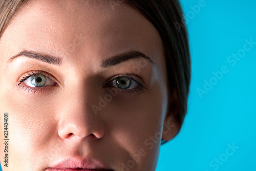 Beautiful Woman Face. Beauty Portrait of young woman brunette smiling on blue background. Perfect Fresh Skin. Youth and Skin Care Concept.