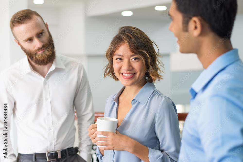 Multiethnic business group chatting during corporate meeting. Cheerful Asian office worker drinking coffee and smiling at camera while her colleagues talking. United team concept Multiethnic business group chatting during corporate meeting. Cheerful Asian office worker drinking coffee and smiling at camera while her colleagues talking. United team concept