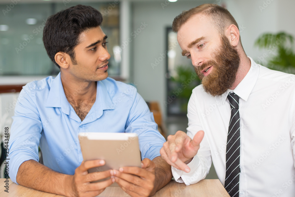 Serious creative professionals studying project. Two employees using tablet and talking. Business app concept Serious creative professionals studying project. Two employees using tablet and talking. Business app concept