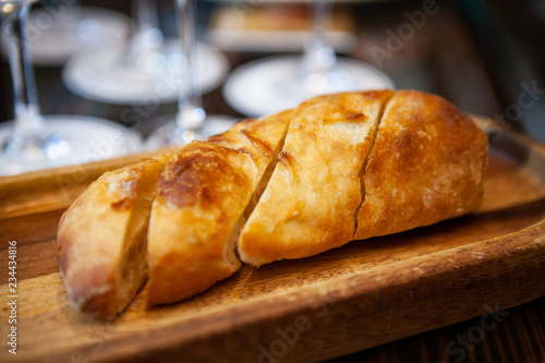 Freshly baked Italian Ciabatta bread from oven on a wooden tray for appetizer or meal starter. Looks tasty and delicious. Good source of carbohydrate. Not gluten-free. Natural light. Selective Focus.