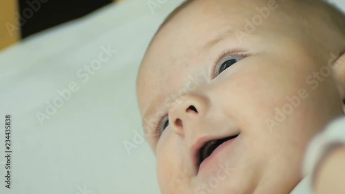 Close-up of a happy newborn baby, smiling while looking into the camera while he is lying in a bed in slow motion.