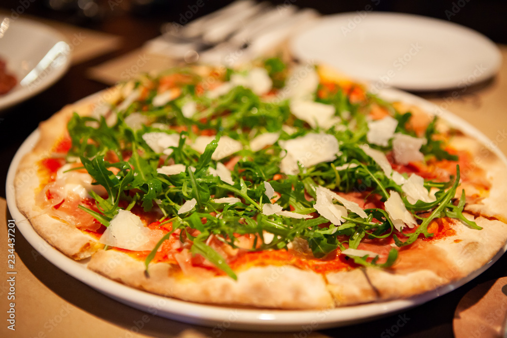 Delicious, cheesy and freshly baked Prosciutto di Parma pizza or pizza with Tomato, mozzarella, prosciutto ham, Arugula and Parmesan cheese. Classic Italian dish. Warm light. Selective focus. Delicious, cheesy and freshly baked Prosciutto di Parma pizza or pizza with Tomato, mozzarella, prosciutto ham, Arugula and Parmesan cheese. Classic Italian dish. Warm light. Selective focus.