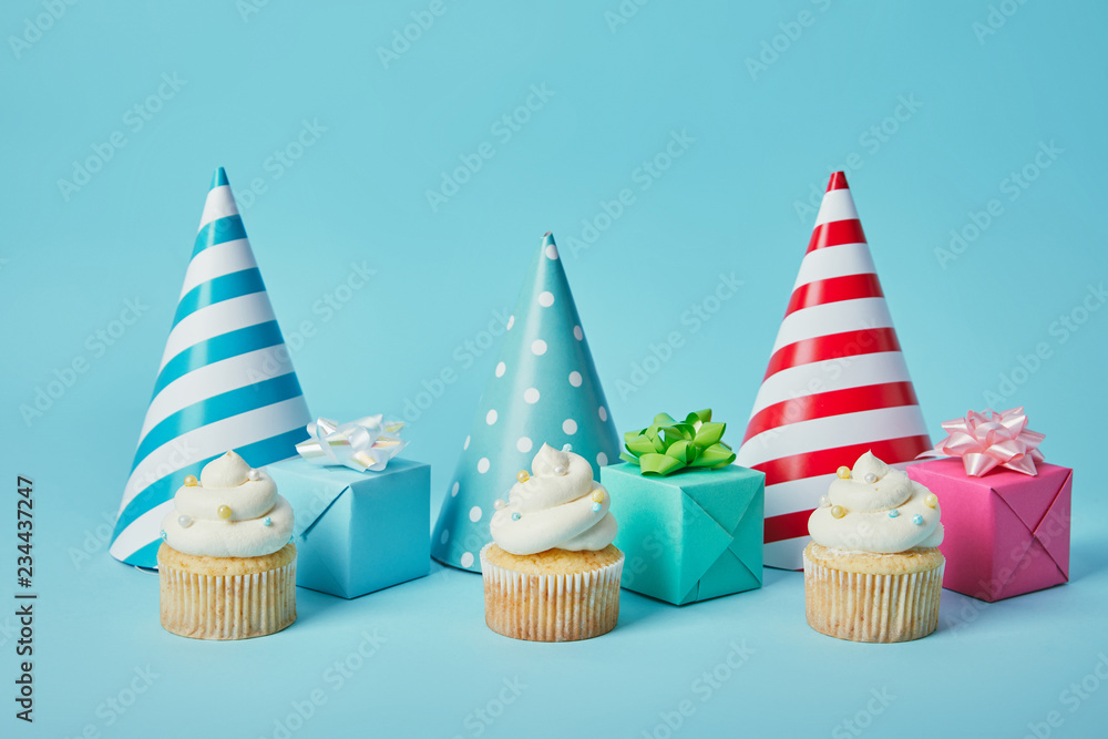 Colorful party caps,gifts and tasty cupcakes on blue background Colorful party caps,gifts and tasty cupcakes on blue background