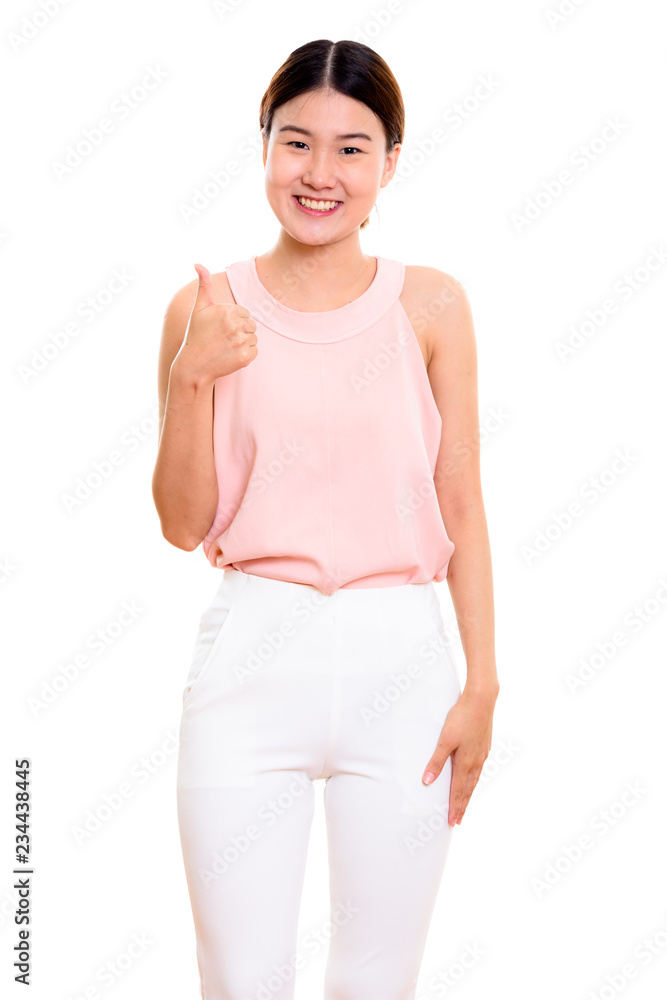 Studio shot of young happy Asian woman smiling while giving thum Studio shot of young happy Asian woman smiling while giving thum