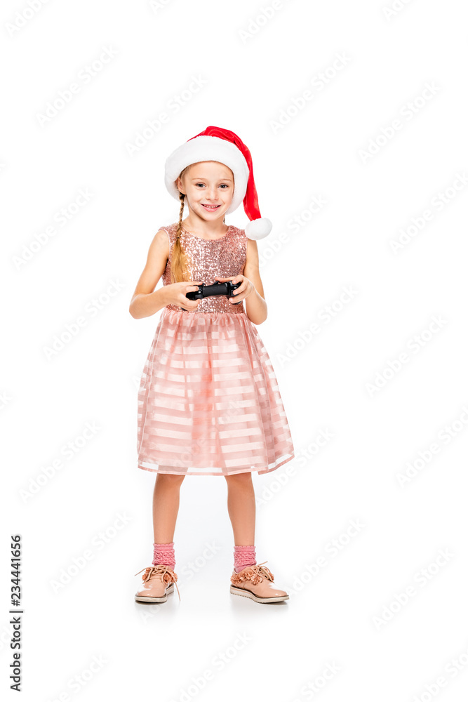 happy little child in santa hat playing video game and looking at camera isolated on white