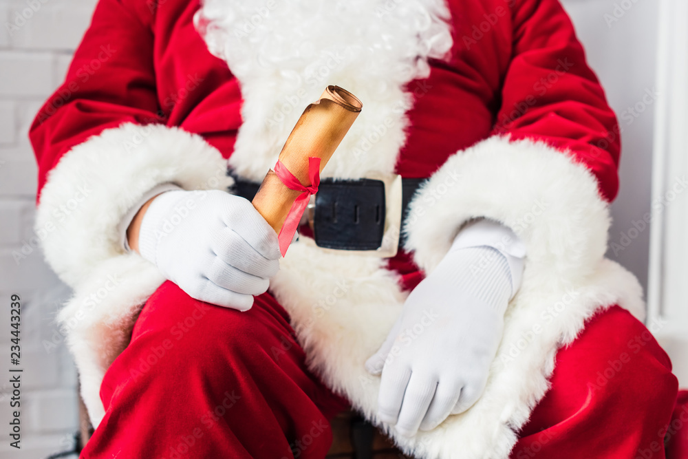 Obraz premium close-up partial view of santa claus holding rolled parchment with wishlist