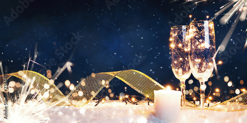 Two glasses filled with garlands with a candle and a gold ribbon in the snow