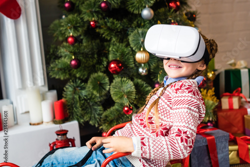 cute smiling child sitting in sled and using virtual reality headset at christmas time