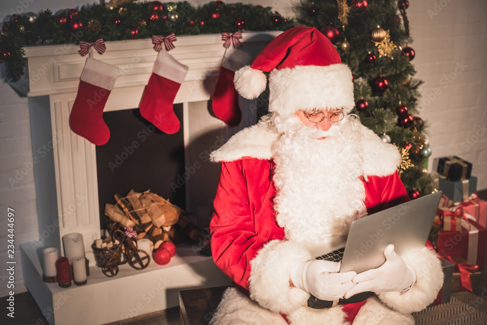 Obraz premium high angle view of santa claus using laptop near fireplace