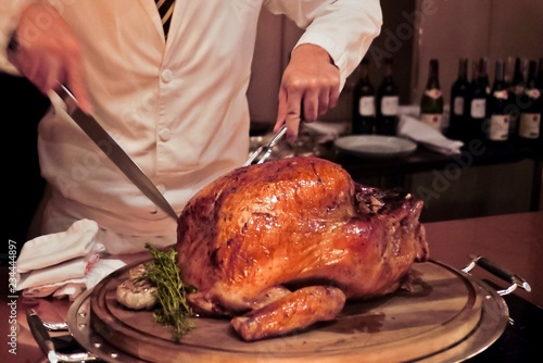 Professional chef carves a whole, roasted Turkey. An impressive centerpiece for family party, Easter, Thanksgiving, Christmas and New Year celebration. Festive holiday and season greeting. Warm light.