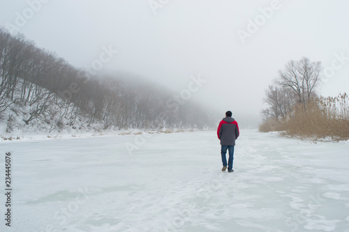 A man walks on a frozen river in winter.