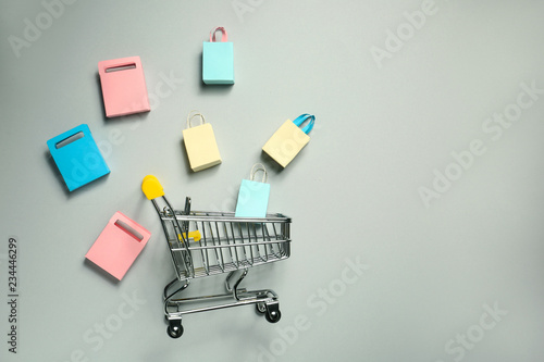Shopping cart with small bags on grey background