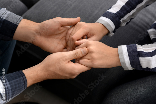 Young couple sitting on sofa and holding hands, closeup