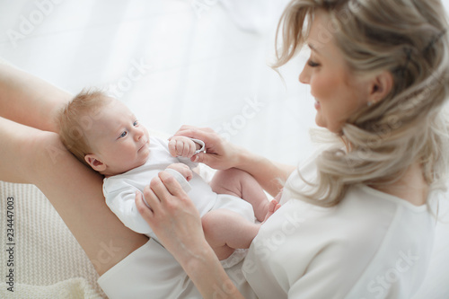 Young mother holding her newborn child.Woman and new born boy relax in a white bedroom.A young mother gently holds her newborn son in her arms.Family at home.Young mother playing whith her newborn son
