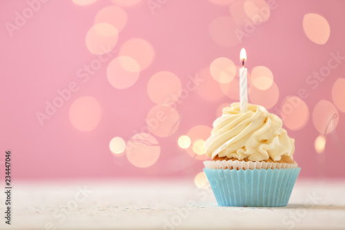Delicious birthday cupcake with burning candle against blurred lights