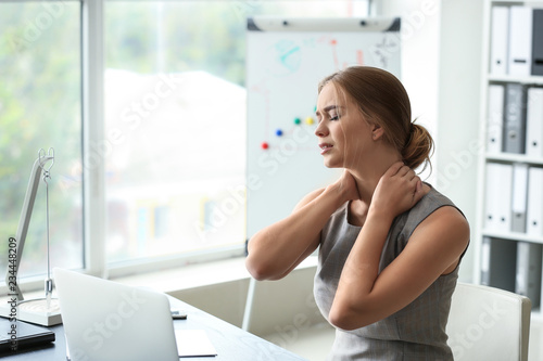 Young woman suffering from neck pain in office photo