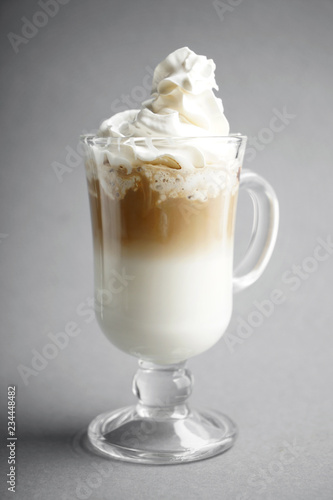 Cold coffee covered with whipped cream in glass on grey background