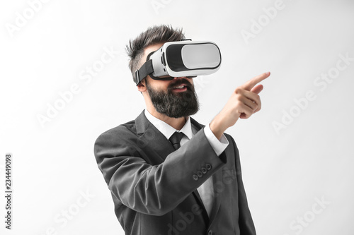 Businessman wearing virtual reality glasses on light background