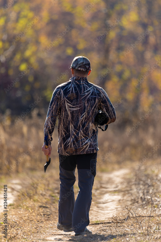 A man in a camouflage suit and an ax in his hand in the fall forest