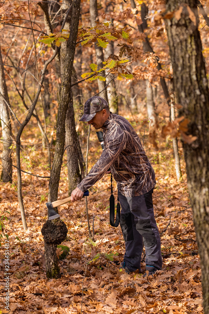 A man in a camouflage suit and an ax in his hand in the fall forest A man in a camouflage suit and an ax in his hand in the fall forest