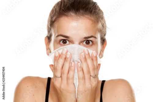 Young woman cleaning her face with wet wipe on white background