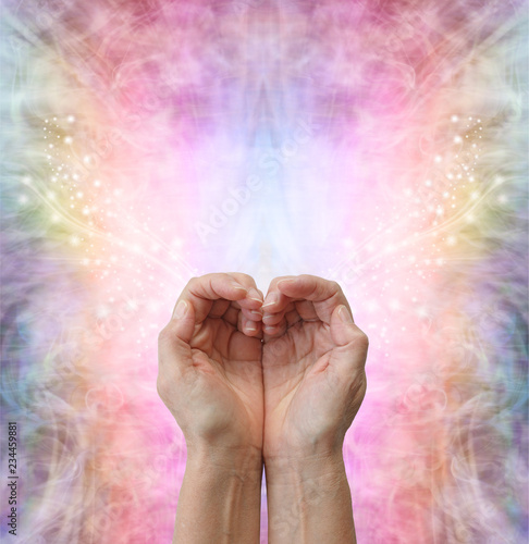 Healers hands making a humble heart shape - female hands in open cupped position creating a heart shape on a rainbow coloured sparkling energy formation background  with copy space above
