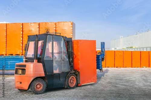 Forklift unloading truck semi trailer with wrapped cardboard boxes outdoors. openair warehouse works background