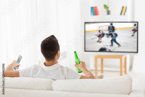 Photography leisure, sport and entertainment concept - man watching ice hockey game on tv an
