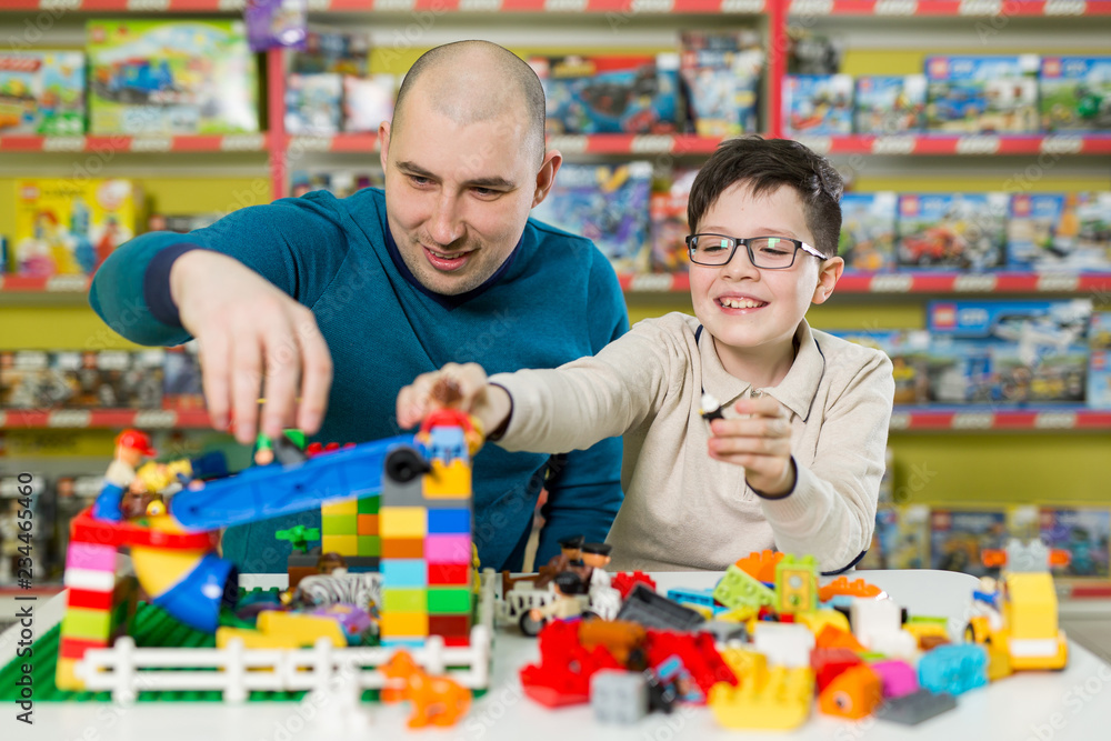 Father and son with happy faces create colorful constructions of toy bricks. Dad and kid build of plastic blocks. Family and childhood concept. Father and son with happy faces create colorful constructions of toy bricks. Dad and kid build of plastic blocks. Family and childhood concept.