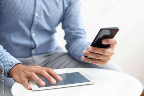 Closeup of man using smartphone and tablet at coffee table. Business man using digital devices. Technology and communication concept. Cropped view.