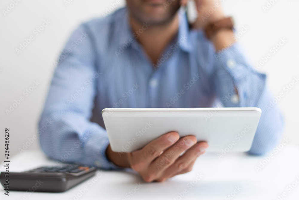 Closeup of man working, using calculator and tablet. Business man calling on phone. Technologies in business concept. Cropped front view. Closeup of man working, using calculator and tablet. Business man calling on phone. Technologies in business concept. Cropped front view.